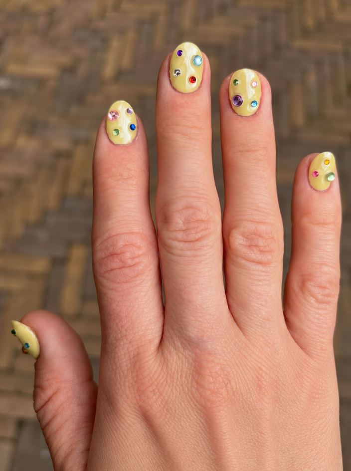 Pale yellow nails decorated with colourful gems